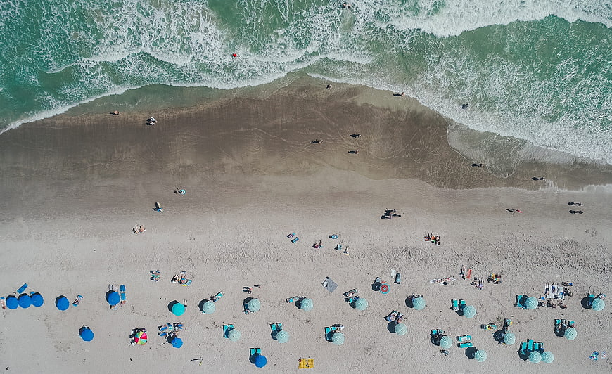 Aerial View of Beach with Blue Umbrellas and Ocean Waves