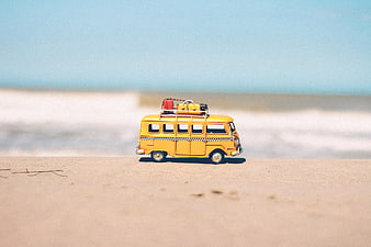 Yellow toy bus on sandy beach with ocean background