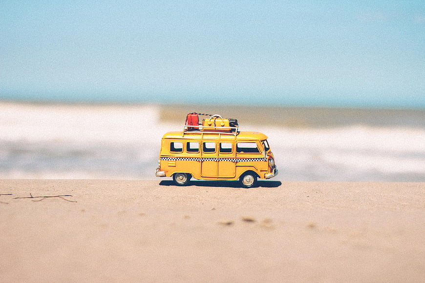 Yellow toy bus on sandy beach with ocean background