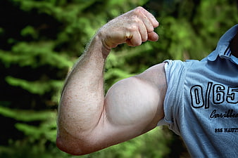 Man flexing bicep muscle outdoors in blue shirt