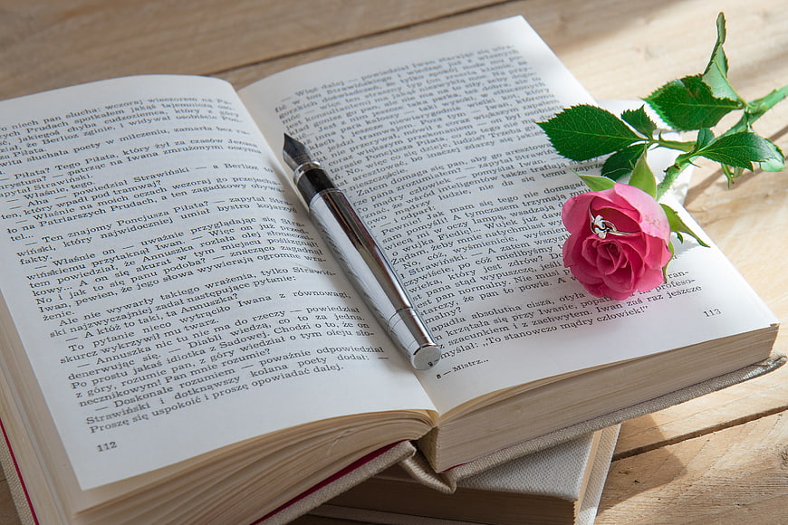 Open Book With Rose And Pen On Wooden Table