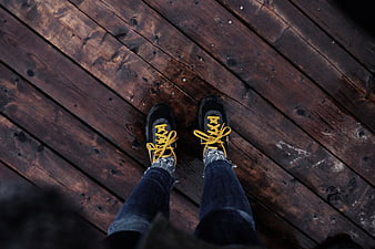 First-person view of black sneakers with yellow laces on wooden deck