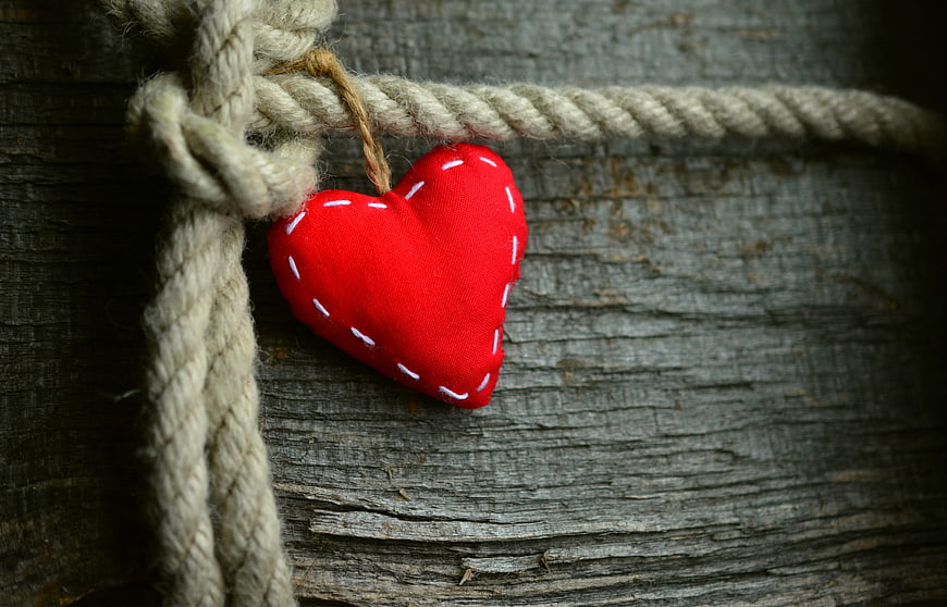 Red Fabric Heart Ornament Hanging on Rope Against Wood