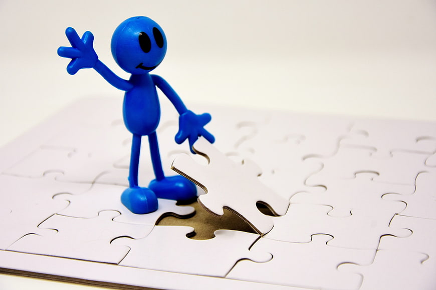Blue figure standing on white jigsaw puzzle with missing piece