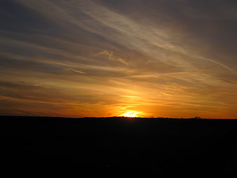 Golden sunset over dark silhouette landscape with wispy clouds