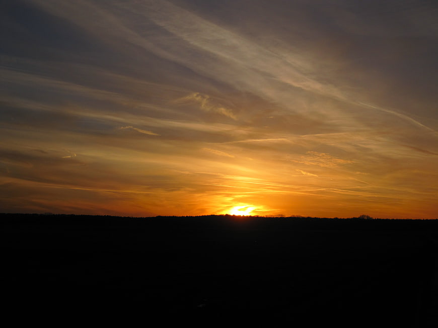 Golden sunset over dark silhouette landscape with wispy clouds