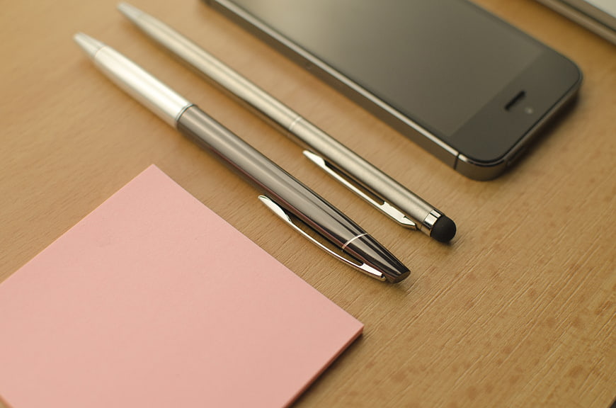 Office supplies with smartphone and pink sticky notes on wooden desk