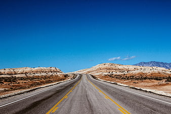 Empty desert highway stretching into the distance under a clear blue sky