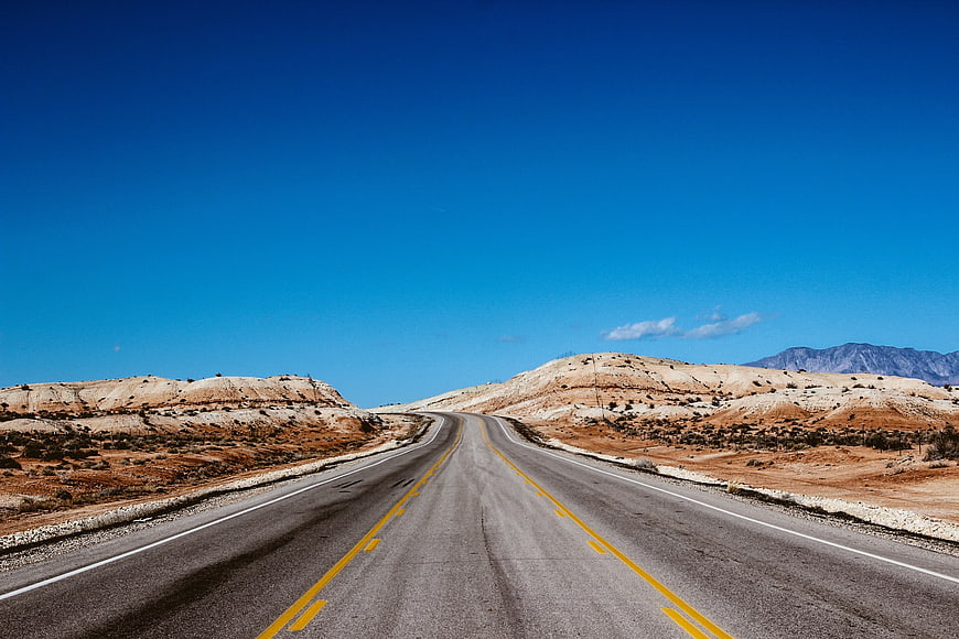 Empty desert highway stretching into the distance under a clear blue sky