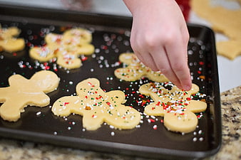 Child decorating gingerbread cookies with sprinkles on baking sheet