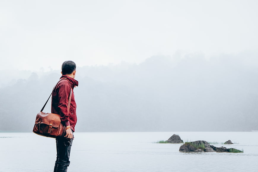 Man with Leather Bag Standing by Misty Lake