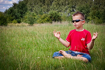 Young boy meditating in a grassy field wearing sunglasses