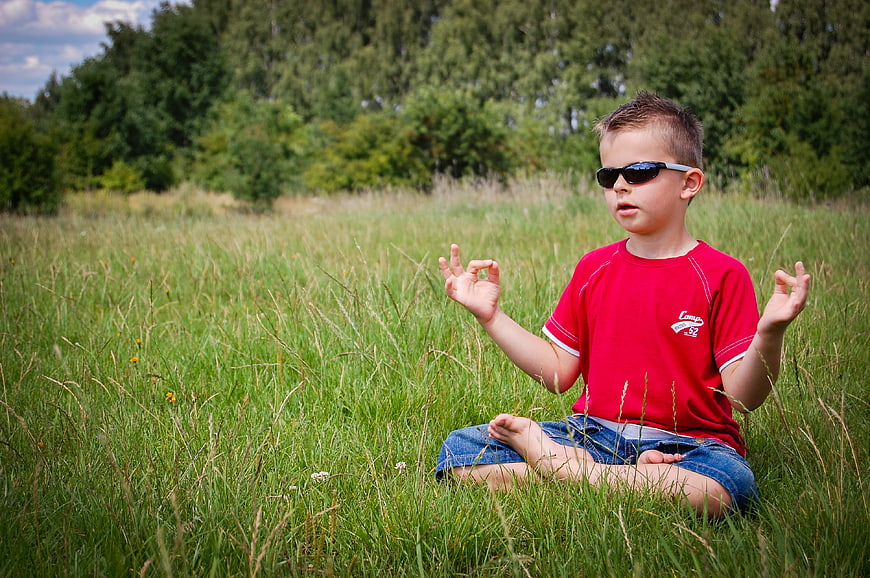 Young boy meditating in a grassy field wearing sunglasses