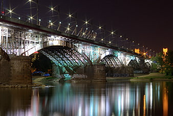 Illuminated Steel Arch Bridge at Night with Water Reflections