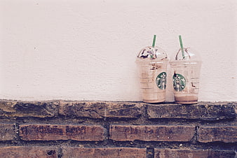 Two iced coffee drinks on a brick ledge against a white wall