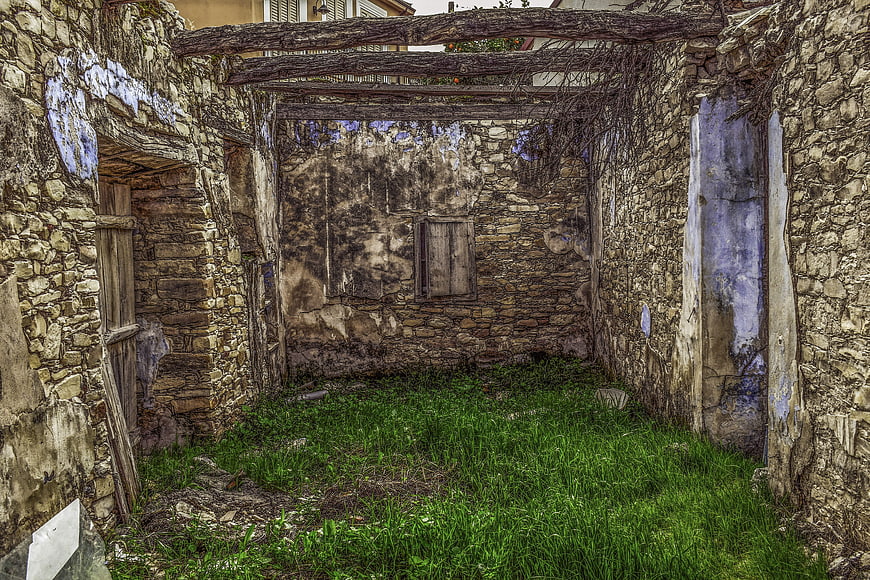Abandoned stone house interior with overgrown grass and weathered walls