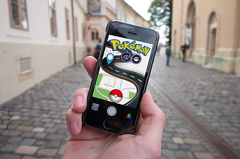 Hand holding smartphone with Pokemon Go game on cobblestone street