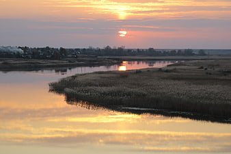 Serene sunset over a winding river with reeds and village reflection