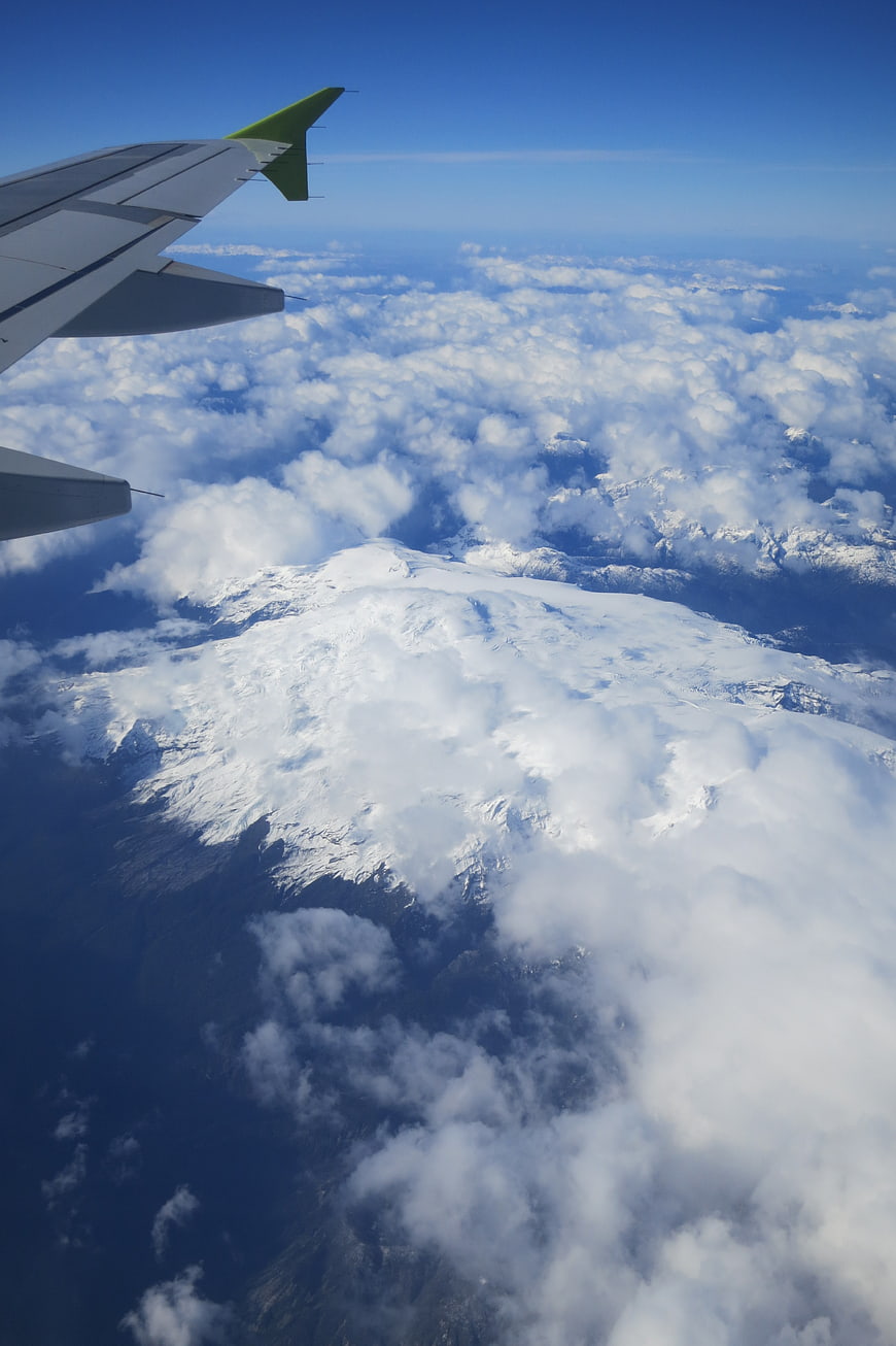 Airplane wing view over snow-capped mountains and clouds