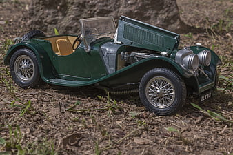 Green vintage model car with open hood on dirt ground