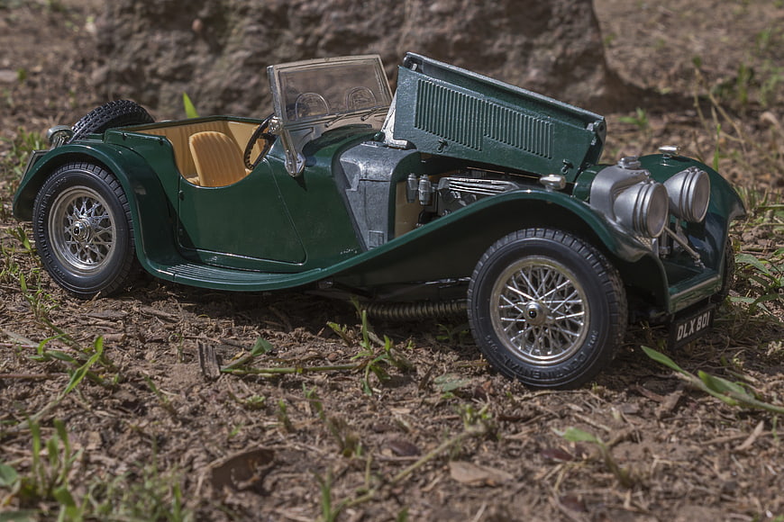 Green vintage model car with open hood on dirt ground