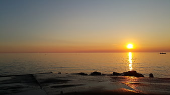 Serene Sunset Over Calm Ocean with Silhouetted Boat