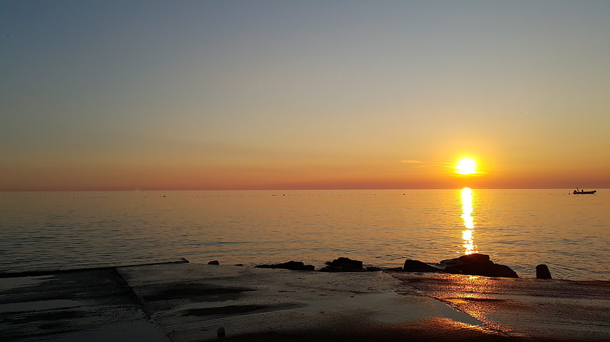 Serene Sunset Over Calm Ocean with Silhouetted Boat