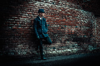 Stylish man in hat and coat leaning against brick wall