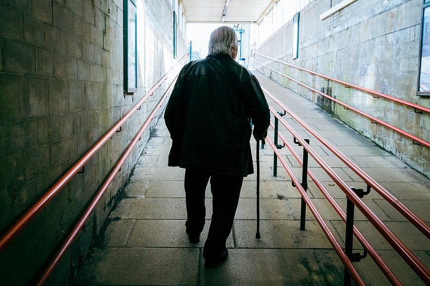 Senior man walking up ramp with cane
