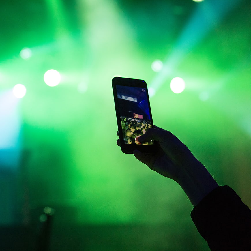 Hand holding smartphone recording concert with green stage lights