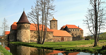 Historic stone castle with red roofs and moat reflection