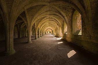 Ancient stone vaulted corridor with sunlight streaming through windows
