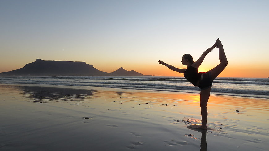 Woman performing yoga pose on beach at sunset with Table Mountain