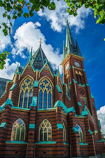 Gothic Brick Church Exterior With Green Spires And Blue Sky