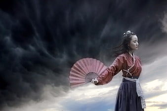 Woman in Traditional Hanfu Holding Fan Against Stormy Sky