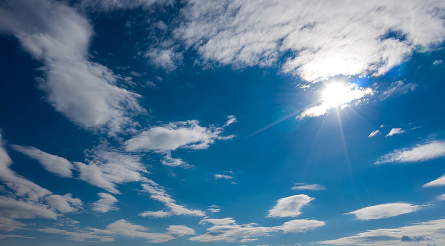 Bright Sun Shining Through White Clouds in Blue Sky