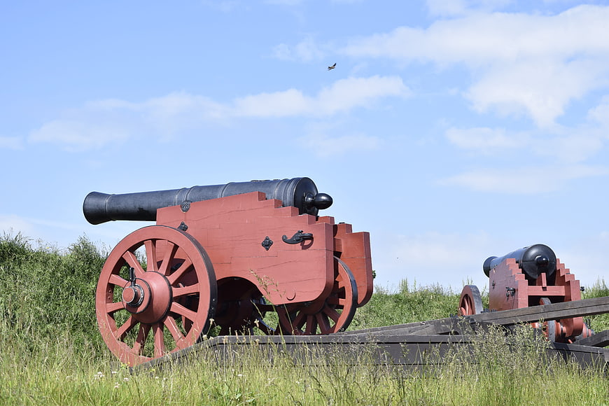 Historic Red Cannon on Grass Field Under Blue Sky