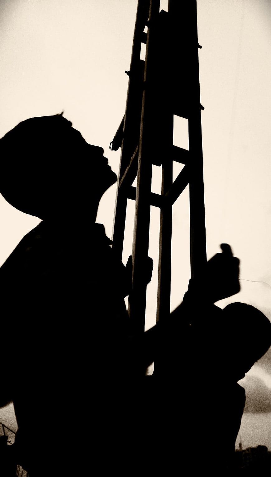 Silhouette of construction workers carrying a ladder