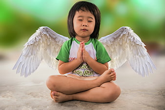 Child meditating with angel wings in a green outdoor setting