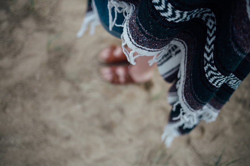 Close-up of patterned shawl and sandals on sandy ground
