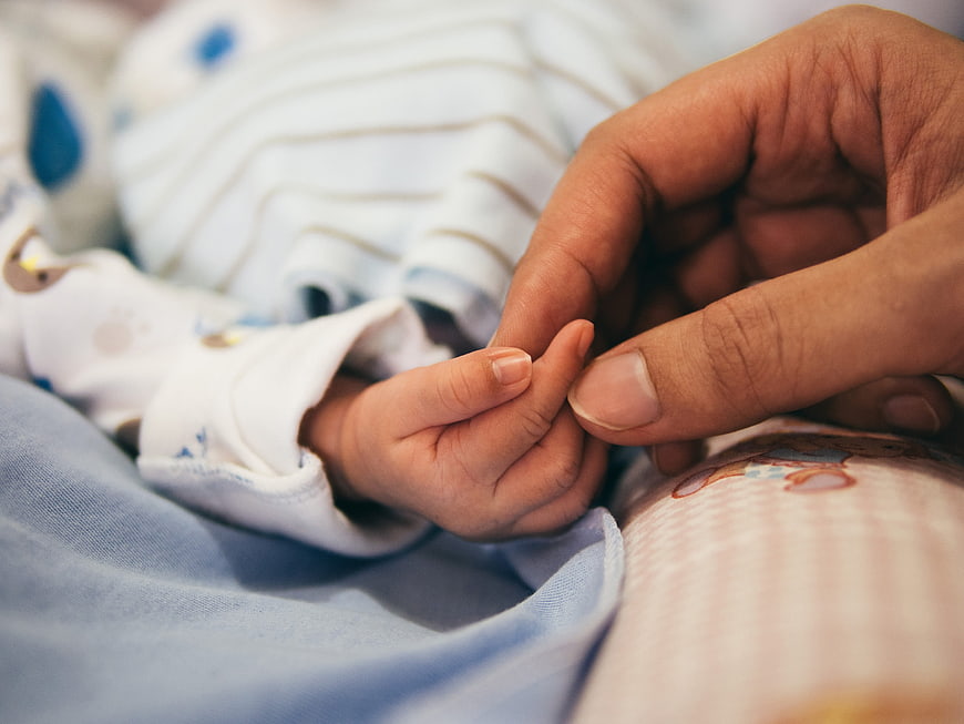Close-up of adult hand holding newborn baby's tiny fingers