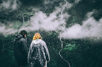 Couple in Raincoats Overlooking Misty Mountain Waterfalls