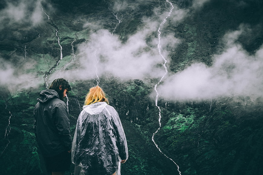 Couple in Raincoats Overlooking Misty Mountain Waterfalls