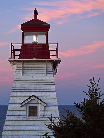 Red and white lighthouse tower against pink sunset sky