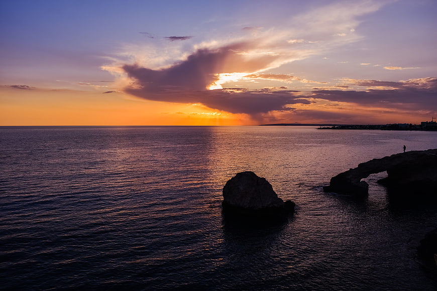 Dramatic Sunset Over Rocky Coastline with Natural Arch