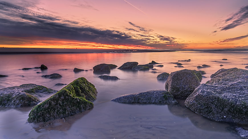Dramatic sunset over rocky beach with long exposure water