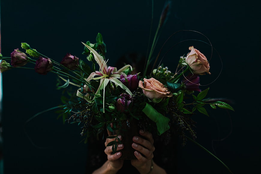 Dark moody bouquet of roses and lilies held by hands