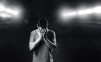 Sad man covering face in rain under stadium lights