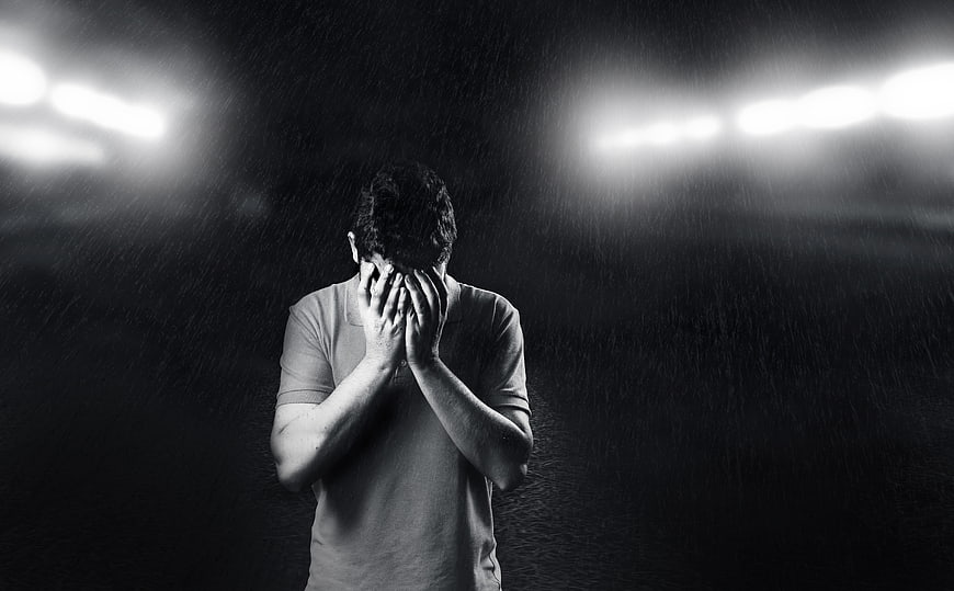 Sad man covering face in rain under stadium lights