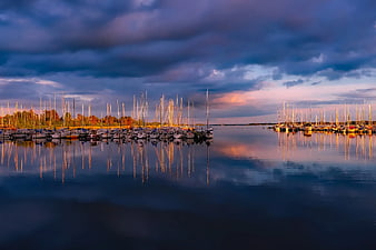 Serene marina at dusk with sailboats and dramatic sky reflections
